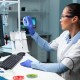 A researcher in a lab analyzes a petri dish, evaluating regenerative therapies like PRP, BMAC, MSCs, Exosomes, and Regenerative Protein Arrays.