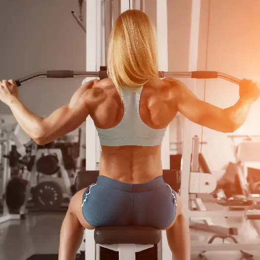 Rear view of a muscular woman performing a lat pulldown in a gym, illustrating how active lifestyle habits affect systemic inflammatory load.