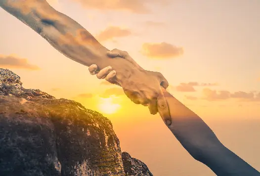 One hand gripping another to lift a climber at sunset, depicting the caregiver burden absorbed by families of chronic patients.