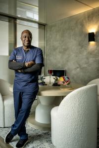 Smiling portrait of Prof. Dr. Bankole A. Johnson, arms folded in blue scrubs, founder of Casa Privée, IRMN, and the Miami Stem Cell Clinic.